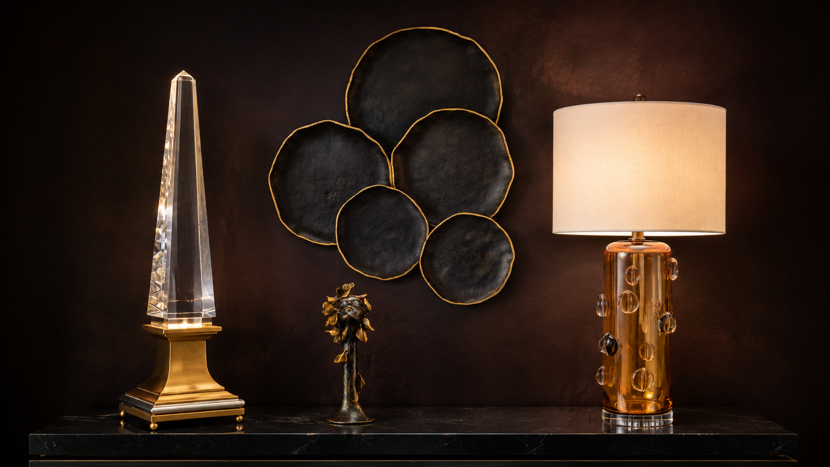 The Gallery: a lit crystal obelisk on a brass base, an amber glass lamp, a bronze sculpture and black-and-gold wall discs on a dark burgundy wall